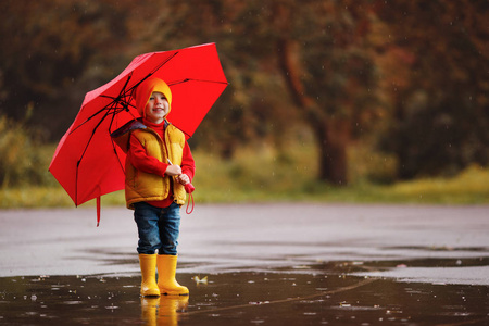 快乐的孩子男孩与橡胶靴和伞跳跃在水坑在一个秋天的沃尔玛