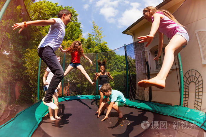 快乐的朋友的肖像, 多民族的男孩和女孩, 跳上后院的蹦床在夏天