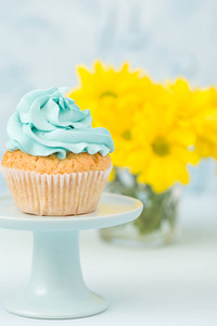 在酒杯花瓶中用蓝色奶油装饰的杯形蛋糕和黄色菊花的花束
