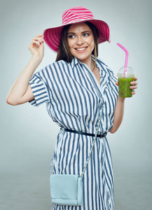 微笑的妇女佩带条纹礼服和夏天帽子藏品玻璃与绿色排毒冰沙饮料