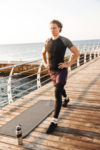 一个专注的运动员的肖像做在健身垫海滩上的运动, 听音乐与耳机