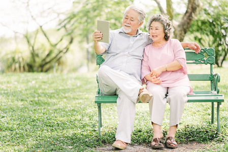 快乐的亚裔夫妇坐在板凳上使用数字平板电脑一起户外