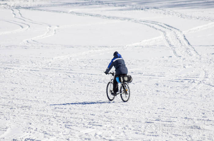 男子骑自行车在冬季在冰雪覆盖的乌拉尔河的冰照片拍摄