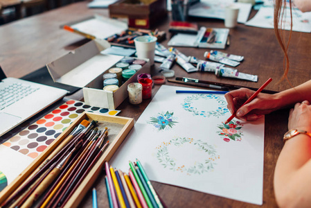 特写女性设计师绘制花卉构图与蜡笔坐在工作场所周围的油漆, 水粉, 刷子和其他艺术用品