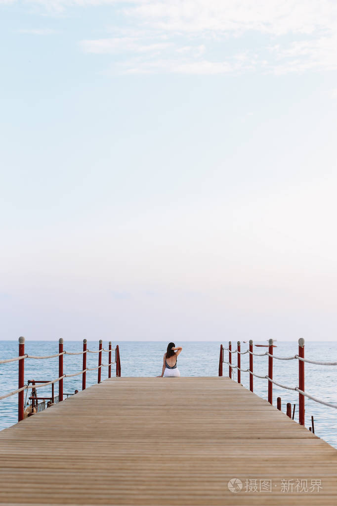 女孩坐在码头上看着海的地平线和蓝天在海上度假夏季时间海洋度假背景