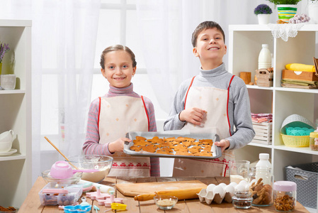 男孩和女孩显示一个托盘烘烤饼干在家庭厨房内部, 自制食品概念