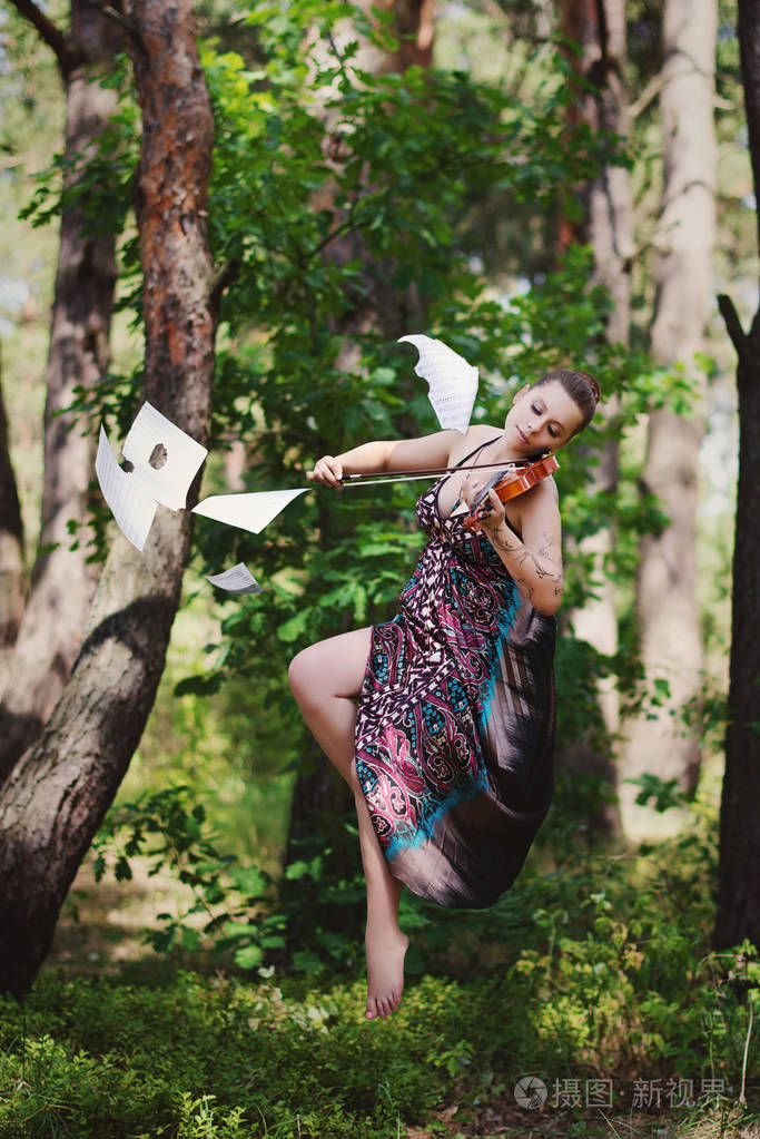 一个穿着长裙小提琴的漂亮女孩在树上徘徊。