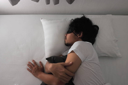 年轻的亚裔男子与面具舒适睡在家里的床上的看法