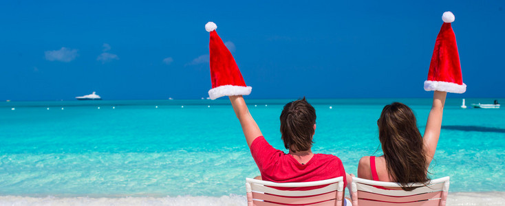 幸福的年轻夫妇，红色的圣诞帽，坐在沙滩椅上