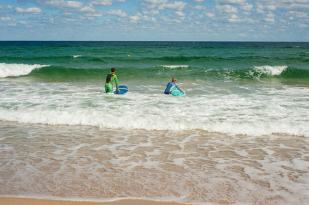 夏天, 女孩和男孩学会在海里骑冲浪板。骑在冲浪板上的海浪在一个美丽的地方。海滩上的冲浪学校