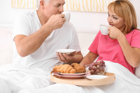 成熟的夫妇在床上吃早饭。浪漫的早晨