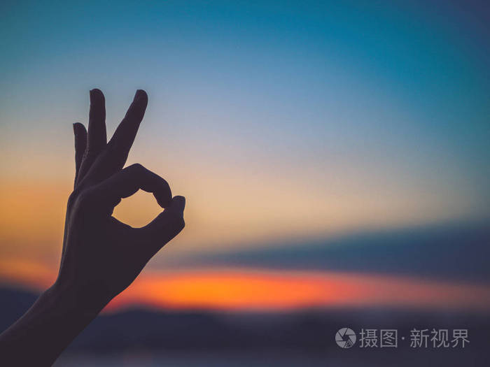 特写和剪影的女人手做 ok 手势在日落背景.希望理念