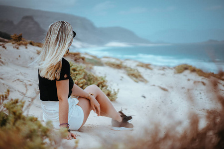 妇女坐在白色沙丘与贫瘠的植被欣赏海岸线景观和大西洋海浪。佛得角圣保罗