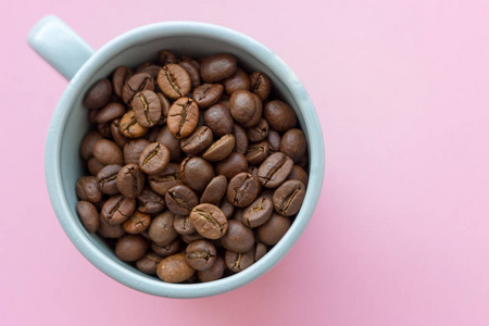 咖啡豆在蓝色杯子在粉红色背景视图从上面。早餐概念与复制空间。咖啡籽特写。早上喝咖啡。咖啡厅理念