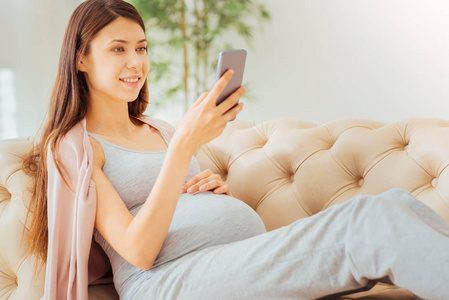 漂亮的产妇使用智能手机躺在沙发上