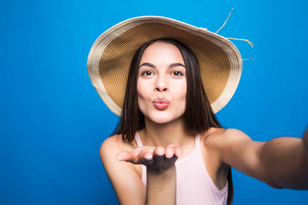 一个快乐的女人在礼服和夏季帽子的肖像采取自拍孤立的蓝色背景