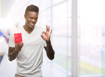 年轻的非洲裔美国男子持有瑞士护照做 ok 标志与手指, 优秀的标志