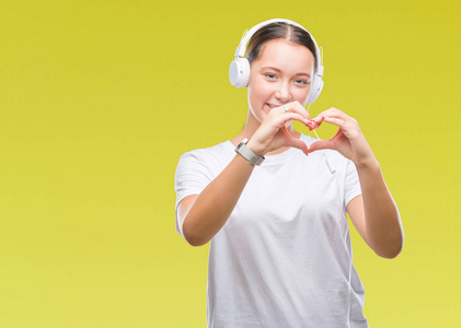 年轻的白种女人听音乐戴着耳机在孤独的背景微笑的爱显示心脏符号和形状用手。浪漫概念