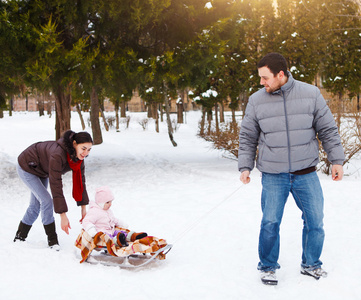 幸福的家庭在冬季公园。雪橇在雪中的宝贝