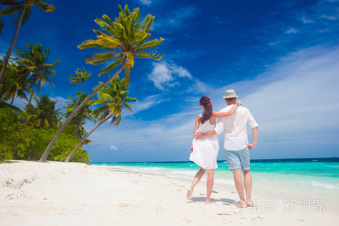 快乐的年轻夫妇穿着白色的衣服在海边散步。马尔代夫