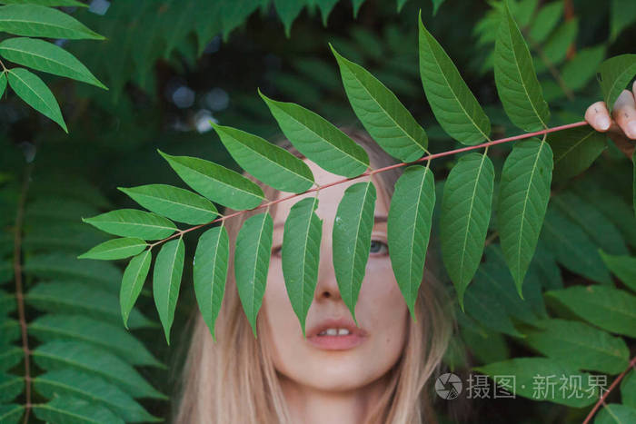 美丽的年轻女人在绿叶的肖像, 金发美女小伙子