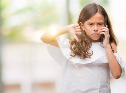 黑肤色的西班牙女孩使用智能手机与愤怒的脸, 消极的迹象显示不喜欢拇指向下, 拒绝概念