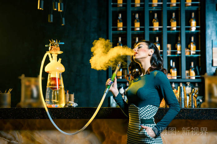 在酒吧后面抽着水烟的年轻女子.烟雾云.享受水烟的年轻女子的美丽肖像