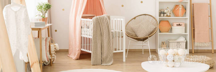 金色扶手椅旁边的白色婴儿床与毯子在粉红色婴儿的卧室内部与梯子
