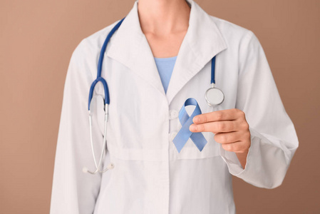 女性医生持有蓝色丝带在颜色背景, 特写镜头。前列腺癌意识概念