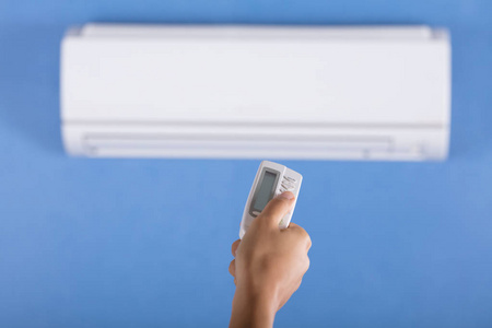 一个人的手操作空调器安装在墙上与遥控