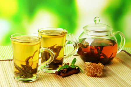 茶杯和茶壶的绿茶加蜂蜜在桌上明亮的背景上