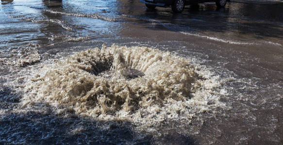 水从道路水舱口流出。水排水喷泉。排系统事故。肮脏的水流喷泉在路上。从舱口喷泉流水