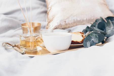 带咖啡和桉树的金色托盘, 干净的白色床上用品。早上好概念