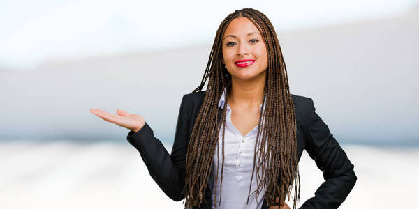 一个年轻的黑人商业妇女的肖像手持东西, 显示一个产品, 微笑和欢快, 提供一个假想的对象