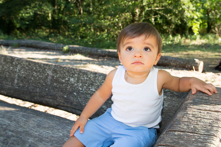 愉快的微笑小男孩摆在木长凳绿色自然公园背景