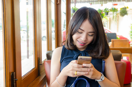 亚洲妇女持有智能手机与微笑脸在咖啡咖啡厅