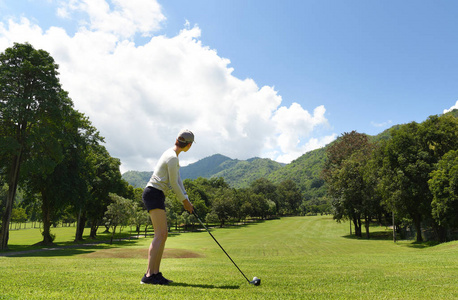 年轻的亚洲妇女打高尔夫球在一个美丽的自然高尔夫球场