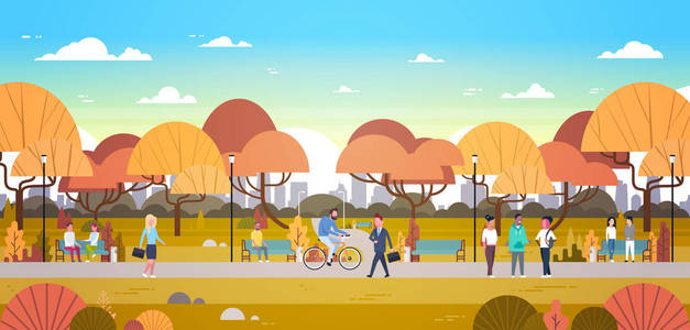 人们放松户外在秋天城市公园在城市天际背景步行骑自行车和通信