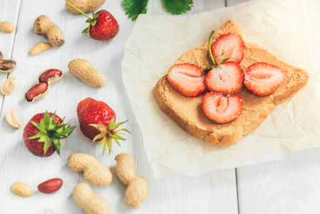 花生黄油三明治与新鲜的草莓在白色的背景。健康的夏日早餐或小吃