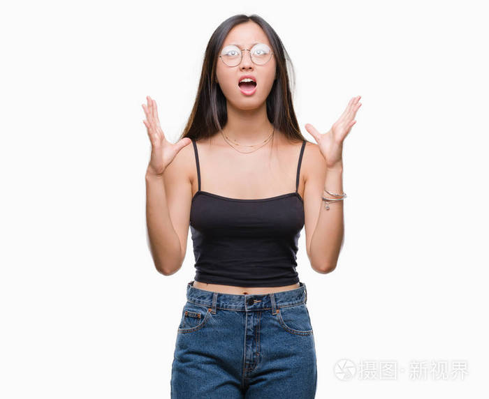 年轻的亚洲妇女戴着眼镜在孤立的背景下疯狂和疯狂的呼喊和激烈的表达和武器大声喊叫。挫折概念