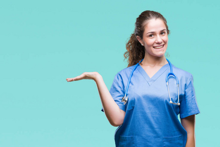 年轻的黑发医生女孩穿着护士或外科医生制服在孤立的背景微笑愉快的介绍和指向用手掌看着照相机