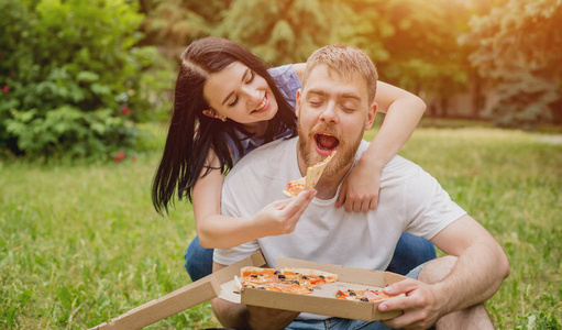 年轻夫妇在公园里吃比萨饼。他们互相款待和欢笑