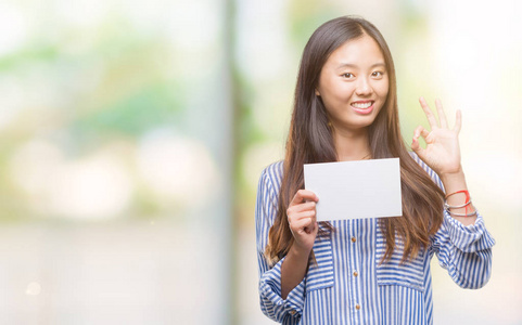 年轻的亚洲妇女持有空白卡在孤立的背景下做 ok 标志与手指, 优秀的标志
