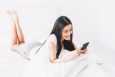 快乐的女人放松和使用智能手机在床上的家庭. 女人用智能手机检查社交应用程序