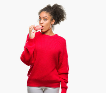 年轻的美国黑人妇女吃甜甜圈在孤立的背景和自信的表情, 聪明的脸认真思考