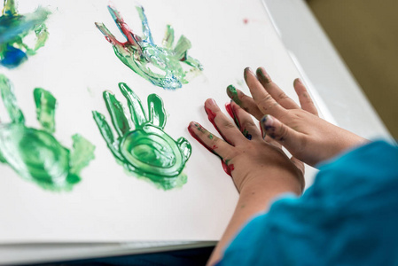 男孩绘画用他的手制作彩色棕榈印在一张纸上