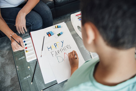 小男孩和他的母亲正在家里用颜料和蜡笔制作父亲节贺卡。