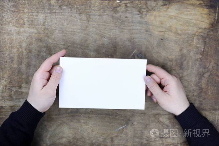男手里拿一张白色的空白的纸上木纹理表格的背景