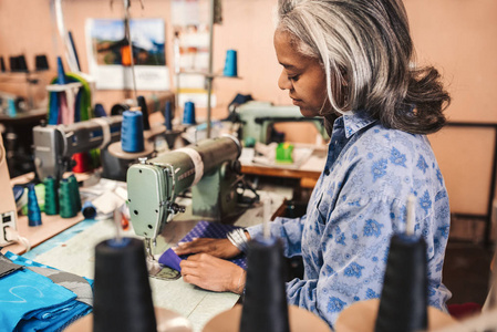 成熟的裁缝使用缝纫机缝制一件五颜六色的织物, 而独自在她的纺织品商店工作