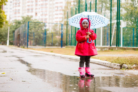 一个可爱的小女孩, 五颜六色的雨伞在雨天在户外的水坑里玩耍